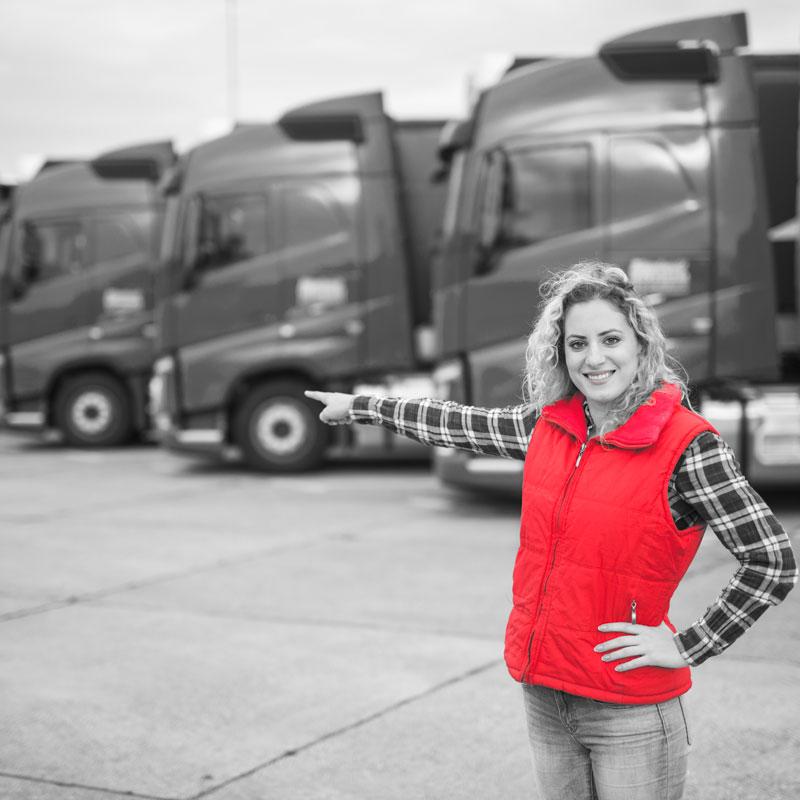 Eine Berufskraftfahrerin zeigt auf eine Reihe von LKWs.